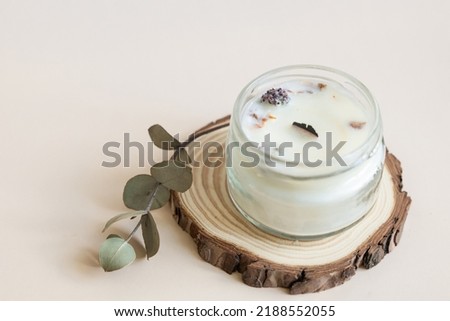 Handmade candle from paraffin and soy wax in glass with wooden wick and dry herbal isolated on pastel beige background. Flat lay, top view, copy space