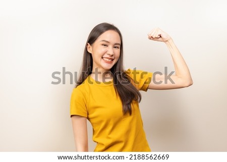 Asian young woman in yellow t shirt doing strong gesture isolated on background.