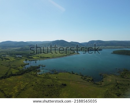 Aerial view on water reservoir at mountain valley covered with green spring forest. Beautiful view from above on smooth blue surface of mountain lake among highlands. Drone point of view. Nobody