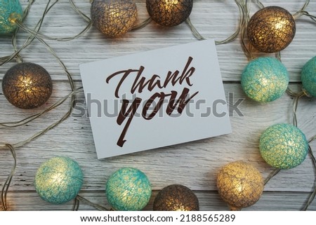 Thank You text on paper card with LED cotton balls top view on wooden background