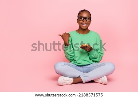 Full size photo of positive lady sit floor look direct finger empty space isolated on pink color background