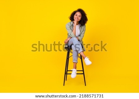 Full body photo of cute young girl wavy hair sit stool smiling banner dressed stylish khaki clothes isolated on yellow color background