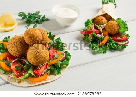 Tortillas, wrapped falafel balls, with fresh vegetables, vegetarian healthy food, on a wooden white background, no people, selective focus.