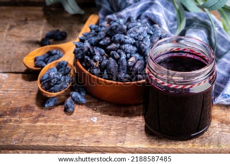 Small glass jar with homemade  haskap berry jam, on wooden background with bowl of fresh haskap (honeysuckle, honeyberry) berries, copy space Royalty-Free Stock Photo #2188587485