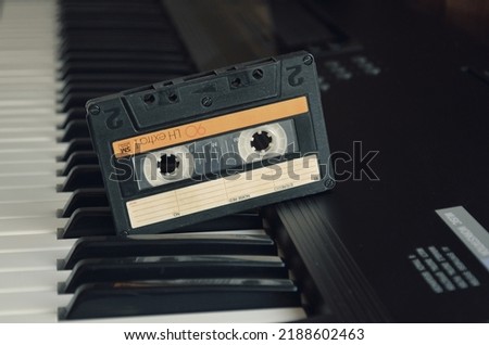 Vintage audio tape cassette on a synthesizer keys from above,Retro cassette.Audio equipment for analog music records. Black stereo tape. Isolated plastic musical device. Old-fashioned mixtape of tunes