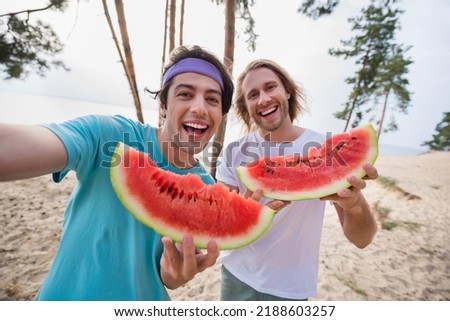 Photo of cool guys eat watermelon do selfie wear casual cloth outdoors near the ocean trees
