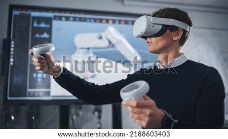 Student Engineer Wearing Virtual Reality Headset Holding Joysticks and Controlling Bionic Limb While Actions Displayed on Screen. Modern Equipment and Computer Science Education in University Concept Royalty-Free Stock Photo #2188603403