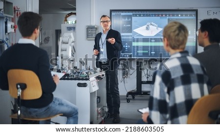 Teacher Holding Microchip for Futuristic Equipment During the Lesson while Robotic Arm Moving Nearby. Diverse Group of Young Engineers Sitting at University. Computer Science Education Concept Royalty-Free Stock Photo #2188603505