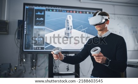 Student Engineer Wearing Virtual Reality Headset Holding Joysticks and Controlling Bionic Limb Under while her Actions Displayed on Screen. Modern Equipment and Computer Science Education Concept