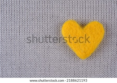 A yellow heart made of wool lies on a gray knitted background with a place for text.Handmade concept, needlework, hobby, sale of yarn for knitting.Cozy background for Valentine's Day greeting cards