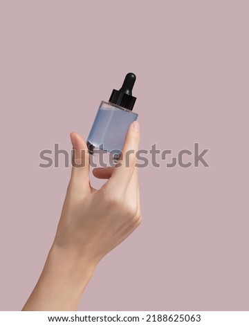 Woman hand holding facial essential oil or serum packaging on pink background. Beauty cosmetic product for skincare concept. Mockup. High quality photo Royalty-Free Stock Photo #2188625063