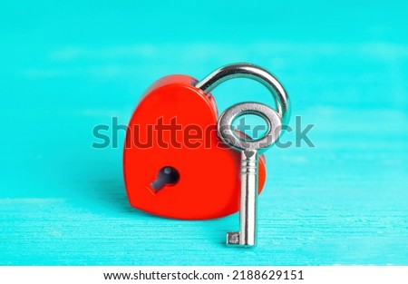 Small red heart-shaped padlock with a silver-toned master key on a blue wooden background. Symbolic romantic concept.