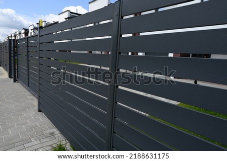 High grey fence. Modern barrier aluminum slats. Modern stone fence with metal shutters. Royalty-Free Stock Photo #2188631175