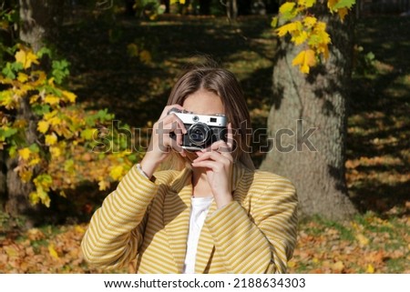 A young girl teenager photographer takes pictures of the autumn park on a vintage film camera.