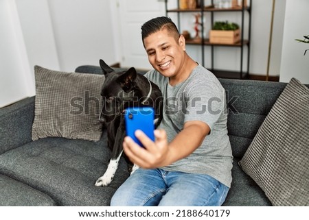 Young hispanic man make selfie by the smartphone sitting on the sofa with dog at home.