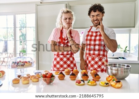 Couple of wife and husband cooking pastries at the kitchen touching mouth with hand with painful expression because of toothache or dental illness on teeth. dentist 