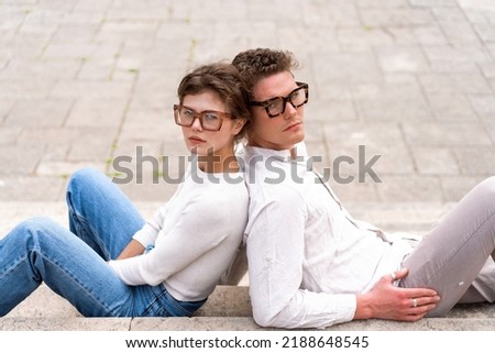 Portrait of two attractive students man and woman wearing stylish glasses sitting floor outdoor and smiling, head to head cheek to cheek, break relax between lesson, work, projects Eyeglasses concept Royalty-Free Stock Photo #2188648545