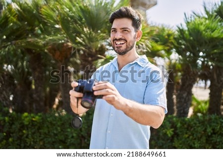 Young hispanic man smiling happy holding professional camera at the city.
