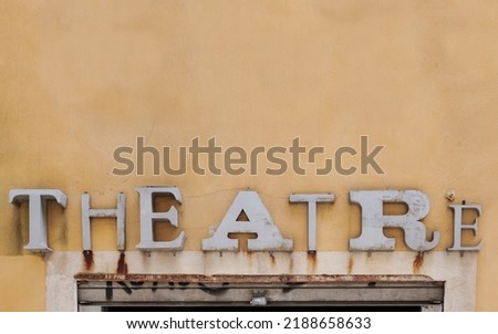 An old rusty sign saying 'theatre' on a yellow wall above the entrance. Abstract background or symbol picture for theaters. Theatre sign in vintage lettering, font style. 