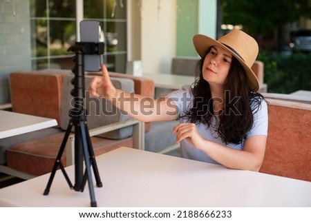 Attractive woman outside sitting with tripod and smartphone,making video call or providing online lesson.