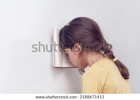 Sad and tired caucasian girl with dyslexia holds a book with her forehead. The child learns to speak and read correctly Royalty-Free Stock Photo #2188671411