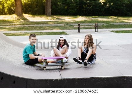 Children with skateboard and penny boards communicate and discuss on the sports playground. Children friendship concept. Children smile and laugh and have fun together
