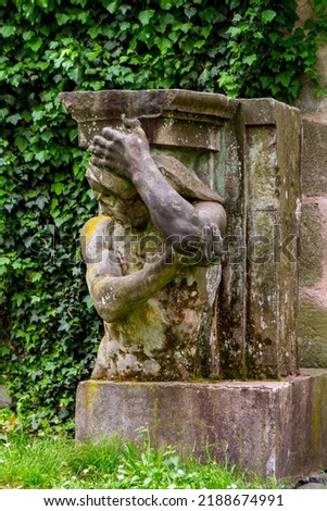 Ancient male carved stone statue in front of medieval pink stone wall in the garden of the Nuremberg Palace, Germany.