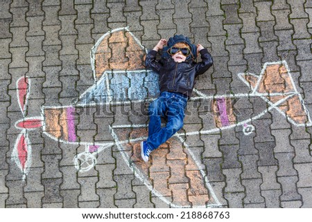 Creative leisure for children: Funny little child of four years having fun with airplane picture drawing with chalk.