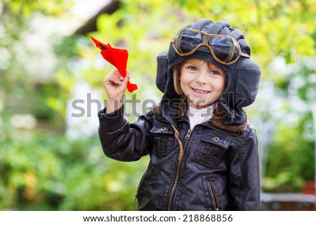 Happy kid in pilot helmet playing with toy airplane against green tree summer background