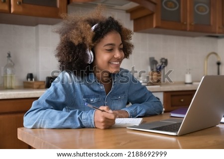 Pretty African girl wear headphones studying sit at table in kitchen use laptop engaged in distancing class with on-line tutor smile enjoy learning feels motivated. Education, video call event Royalty-Free Stock Photo #2188692999