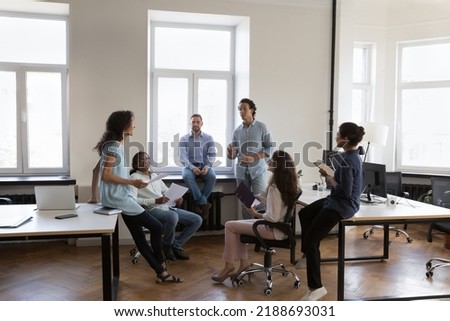 Multiracial staff members, colleagues talking about new project, brainstorming, gathered in coworking workspace. Share knowledge, information or ideas, cooperate, take part in morning briefing Royalty-Free Stock Photo #2188693031