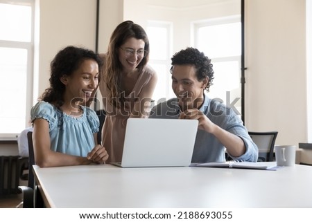 Three multiracial colleagues use laptop speaking on project, discuss collaborative task, learn new software, enjoy amusing content during break at workplace. Teamwork, cooperation, modern tech Royalty-Free Stock Photo #2188693055