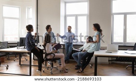 Multiethnic staff members gathered in coworking solve business, listen to male team leader during morning briefing in modern company office. Boss share information, corporate goals, tell about Royalty-Free Stock Photo #2188693103