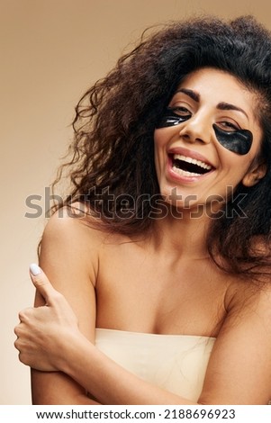 Cute laughing happy pretty Latin female with black hydrogel patches under eye hug herself posing isolated over pastel beige background. Cosmetic product ad Natural beauty concept Studio portrait