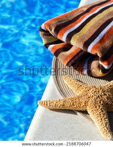 A big starfish and a colorful towel next to the pool. Multicolored bath towel against blue water background.