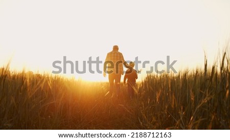 Farmer and his son in front of a sunset agricultural landscape. Man and a boy in a countryside field. Fatherhood, country life, farming and country lifestyle. Royalty-Free Stock Photo #2188712163