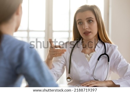 Serious female doctor wearing white uniform with stethoscope consulting patient at medical appointment in hospital, physician therapist gp giving recommendations to young woman at meeting Royalty-Free Stock Photo #2188719397