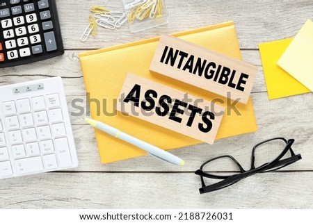 Intangible assets text on wood block on yellow notepad Royalty-Free Stock Photo #2188726031