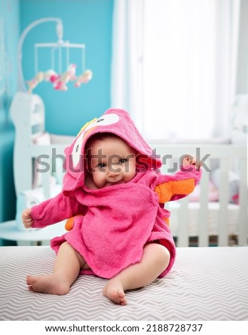 Little baby on a pink baby robe with owl hood, on a child bedroom background
