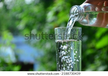Drink water pouring in to glass outdoor over sunlight and natural green background on white table