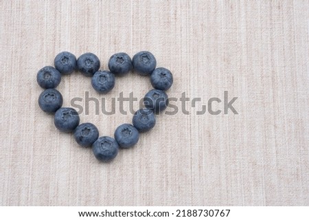 Heart of single blueberries on linen cloth. Tiny blue fruits arranged in the shape of a heart. Summer fruit on fabric.