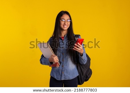 Young student holding backpack, books and looking at cellphone in studio photo