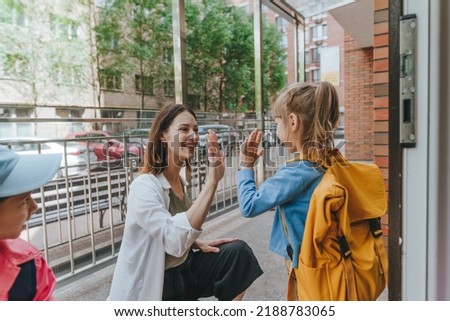 Happy smiling woman teacher greeting elementary school students giving high five at first day at school standing near the open door outside. Selective focus. Royalty-Free Stock Photo #2188783065