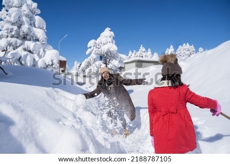 portrait of asian mother and daughter playing snow fight during winter