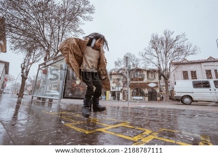 girl playing hopscotch on sidewalk during winter and snow fall