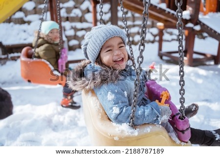 close up portrait of a cute little girl smiling while swinging in the playground full snow in winter