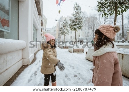 two little girl fighting snow ball in the city during winter