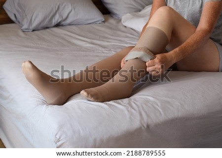 Woman sitting on bed putting on compression stockings on her legs