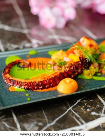 Colorful seafood appetizer. Grilled octopus on the plate on black marble background. Exotic cuisine. 