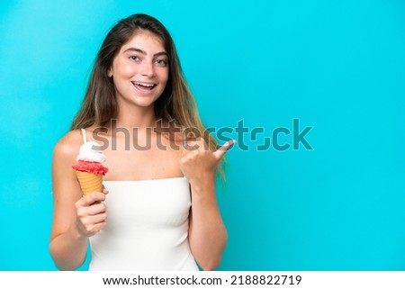 Young woman in swimsuit holding an ice cream isolated on blue background pointing to the side to present a product